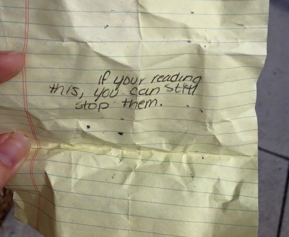 A crumpled yellow paper with blue lines that reads “if you’re reading this, you can still stop them.”