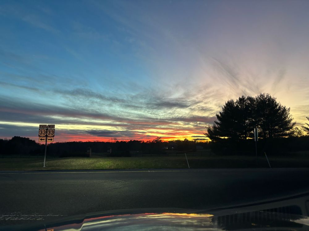 Sunset showing streaming clouds, tree and a highway sign in car headlights 