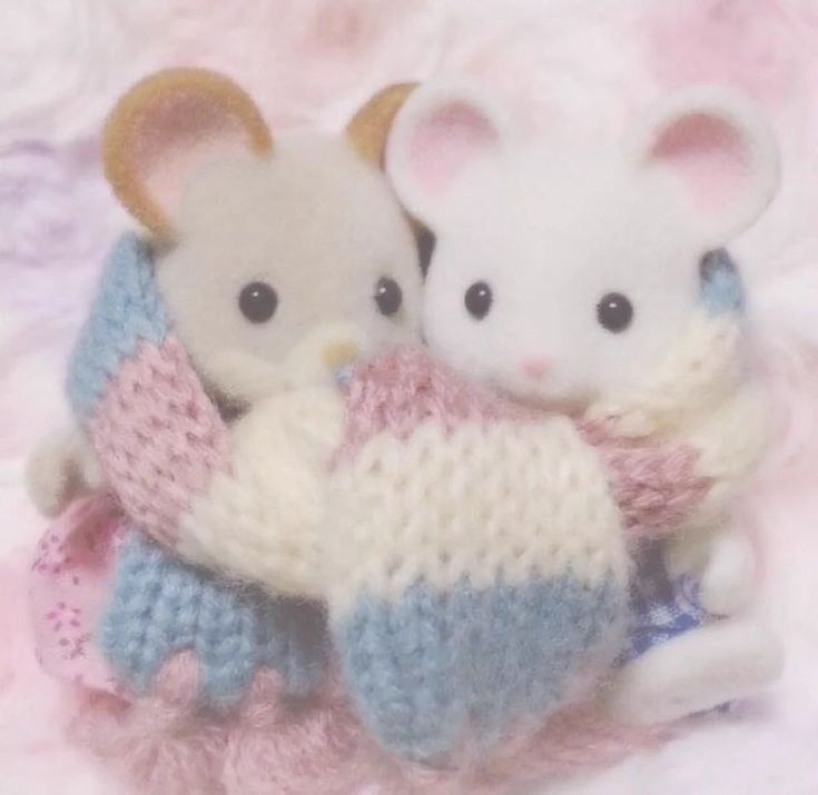 An image, acquired via Pinterest, of two small Calico Critter figurines sitting together while bundled up in a striped scarf they’re sharing that has pink, white, and blue stripes 