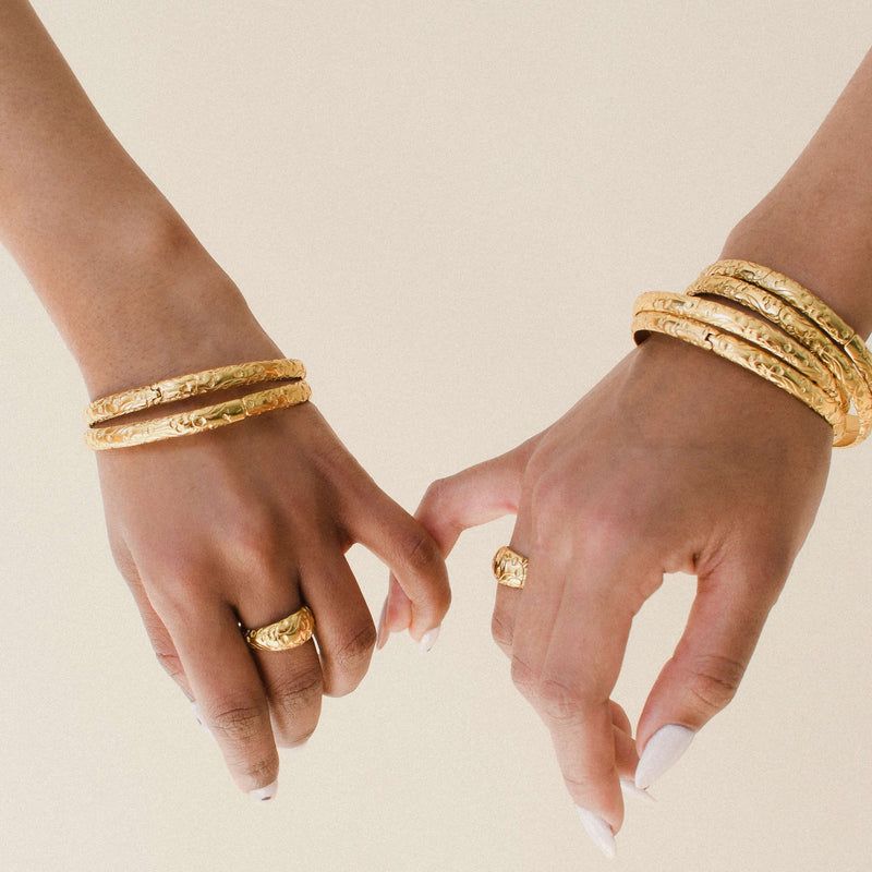 A close-up image against a pale background with (presumably) two desi women’s hands linking by their pinky fingers, as they model BySimran’s rani bangles on their wrists and rani dome rings on their fingers; not my photo, this image is featured on the BySimran website, all credits to BySimran and their models 