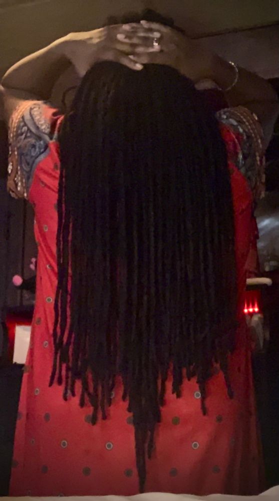 In a snapshot, I am faced away from the camera, in a red pattern gown. I am holding my loc'd hair at it's roots while they cascade down my back.