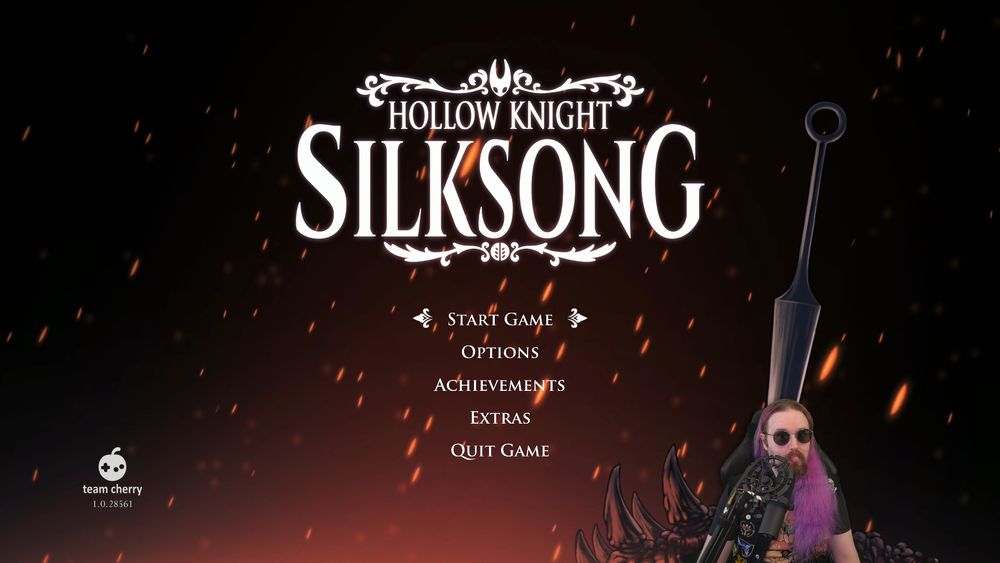 Will, a purple haired streamer with dark glasses, sits in front of the Hollow Knight Silksong starting screen.