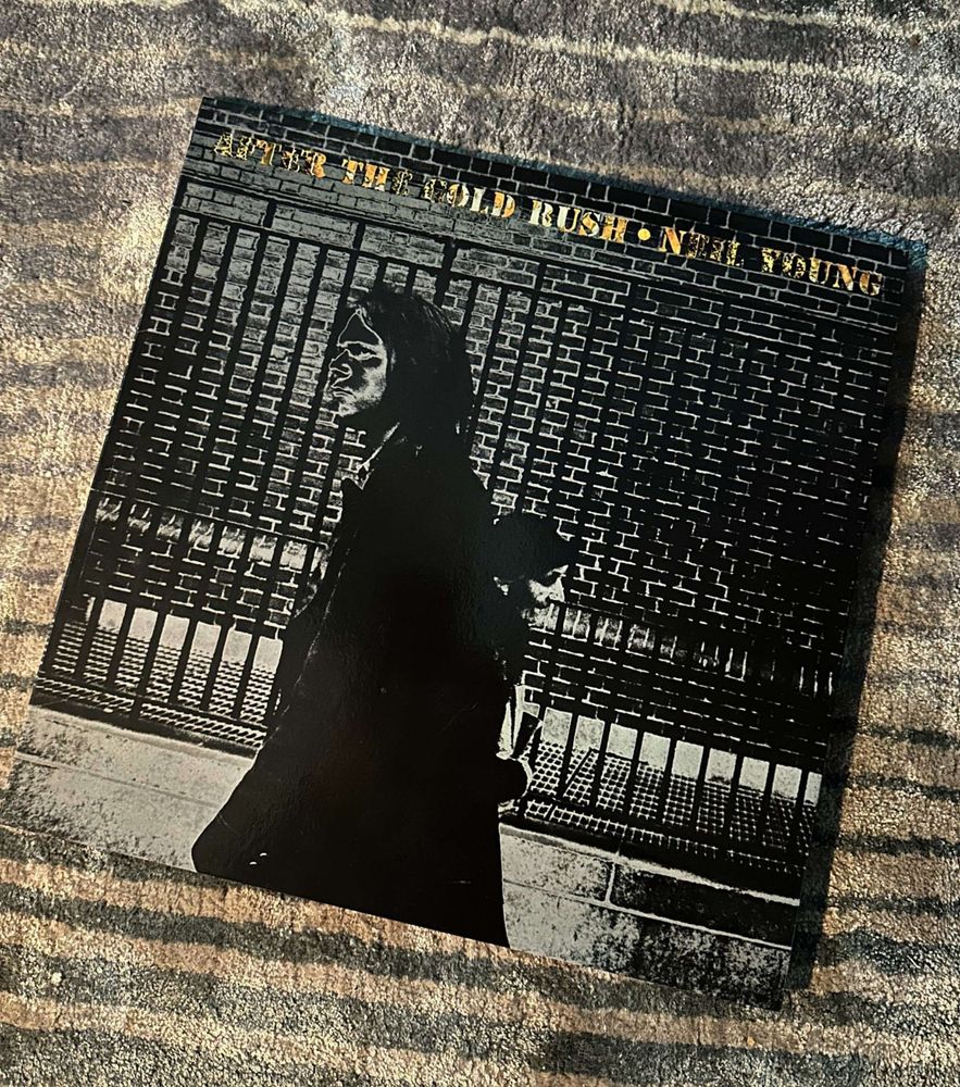Album cover of Neil Young's "After the Gold Rush," featuring a black-and-white image of a figure walking by a brick wall and fence.