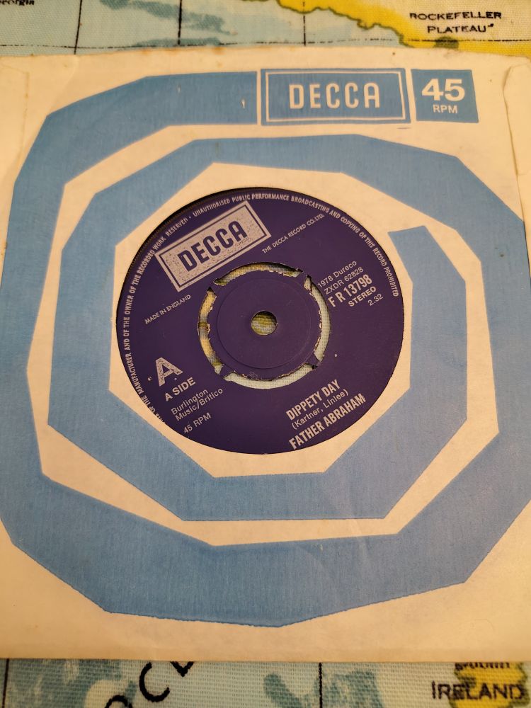 The 7" single Dippety Day by Father Abraham, with a dark blue label, in a paper sleeve with a light blue swirled pattern and DECCA 45rpm on its top right.