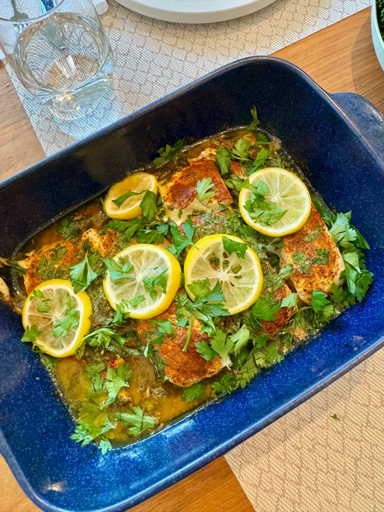Fish cooked in a dish with a lot of lemon slices, herbs and spices