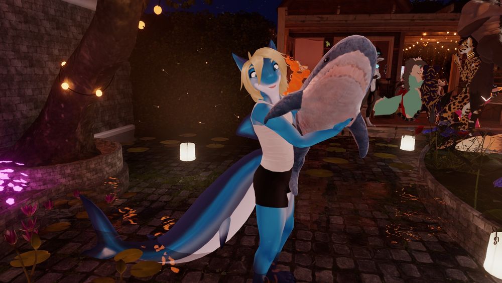 a blue anthropomorphic mako shark boy with blonde shaggy hair named "Time" presenting a Ikea blahja in vr chat while smiling, looking at the viewer and sticking his tongue out in a playful manner. He stands at five three with a rather large six foot shark tail and rudder. Time is wearing a simple tank top and latex short shorts letting his built thighs stay in plain view. He is in a large outside pond with ankle high water with some other anthropomorphic animals in the background and fire flys through out the picture providing the lesser half of the lighting. A large tilted tree looms over the lesser mako shark and has a few round lights wrapped and hung from it. lanterns and lilly pads float about with some budding flowers in the dark of night.