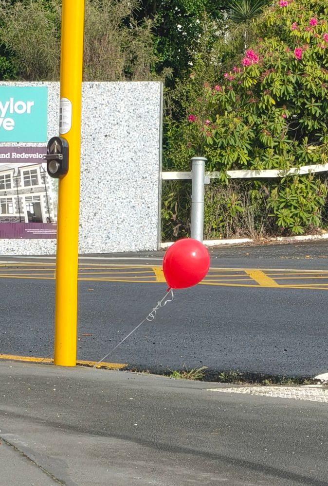 A red balloon waves enticingly from a grate at an intersection. 