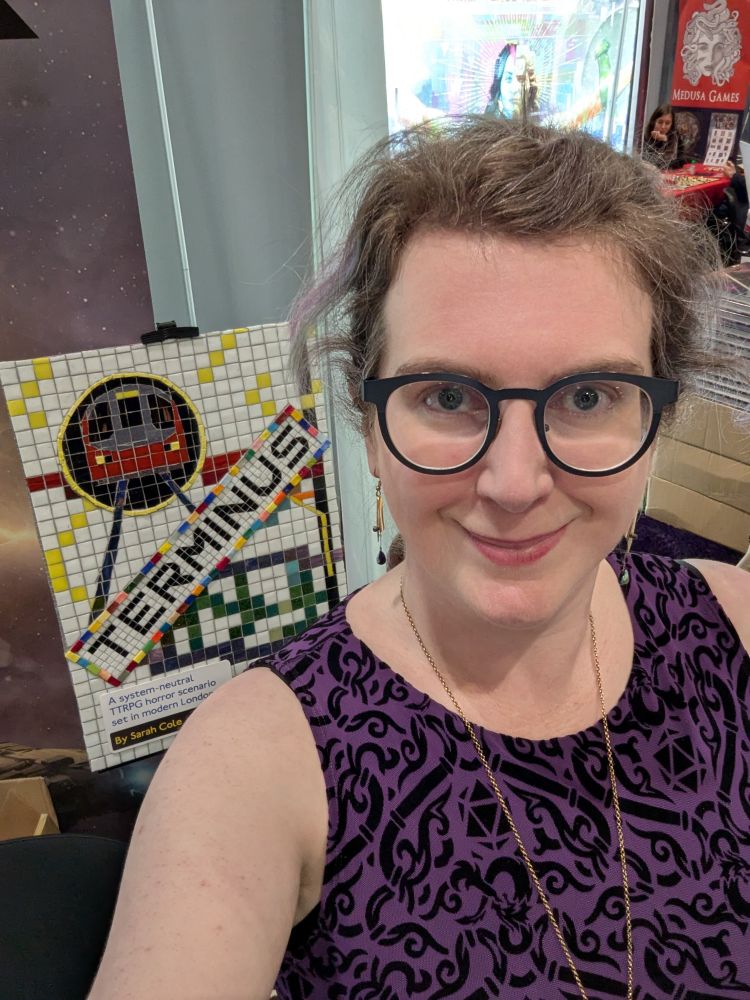 It's me! My hair is tied back, and I'm wearing a purple dress. Behind me, the TERMINUS cover art mosaic lurks on an easel. 