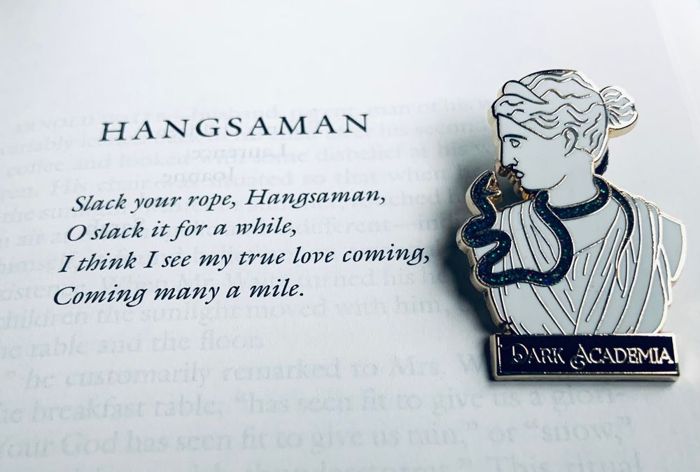 Pictured is the opening page of the novel Hangsaman with a Dark Academia pin (showing a classical bust encircled by a snake) resting on it. 