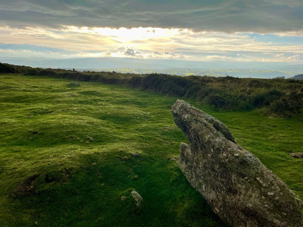 Beneath lowering clouds, a wide strip of blue sky lets through the sunshine onto Dartmoor.