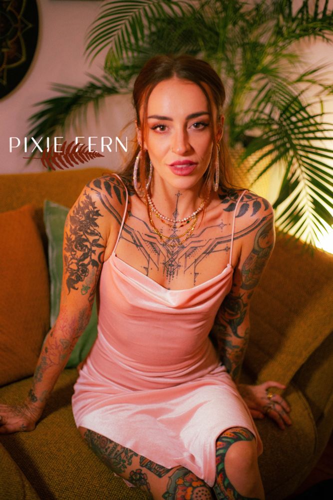 Pixie sits on a mustard armchair, wearing a baby pink velvet slip dress, gold and pearl necklaces and diamanté hoops. Her hair is pulled back and she’s gazing into the camera, with a backdrop of golden light and palm leaves. 