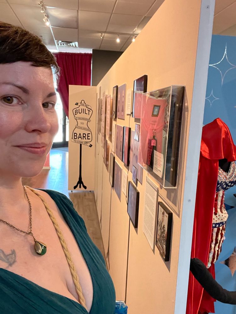 Christina stands in front of a wall display at the Burlesque Hall of Fame. In the basic ground, the words “Built to Bare” are visible.