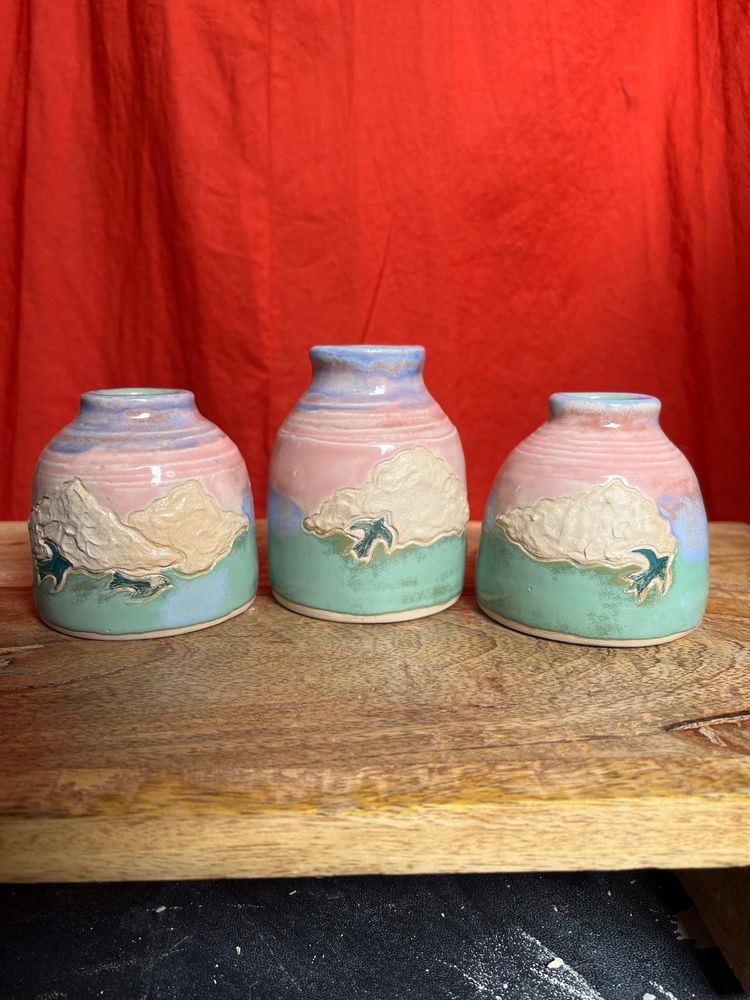 Small bud vases with green, pink and blue sunsets. Clouds embossed in the middle of each vase with birds flying over them. 