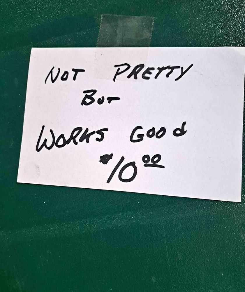 White card taped to a green camp stove. Text says not pretty but works good $10
