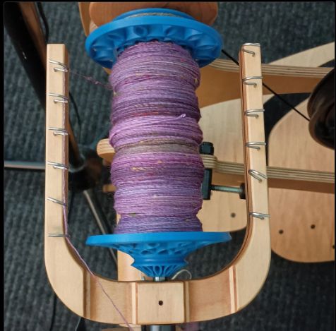 Purple yarn single on a blue bobbin. 