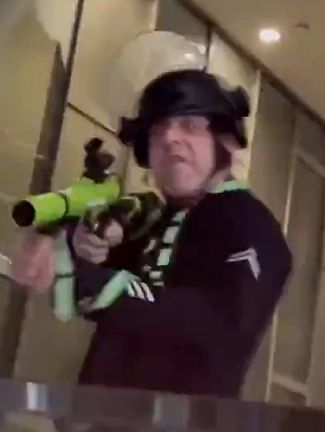 LAPD pig Rick J Linton, 40mm grenade launcher at the ready, looking like a fascist zombie with glowing red eyes.