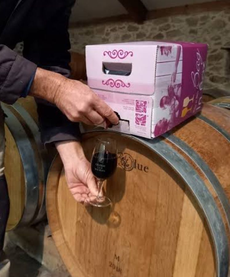 Deux mains se servant un verre de rouge depuis un cubi de rouge posé sur un tonneau. Toute ressemblance avec Charlie Kirk est fortuite