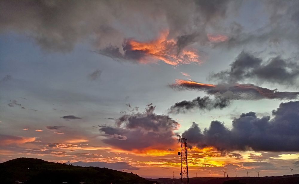 Blue , orange and gray sunset sky with silhouette of dark hill, metal tower and distant windmills in the background.