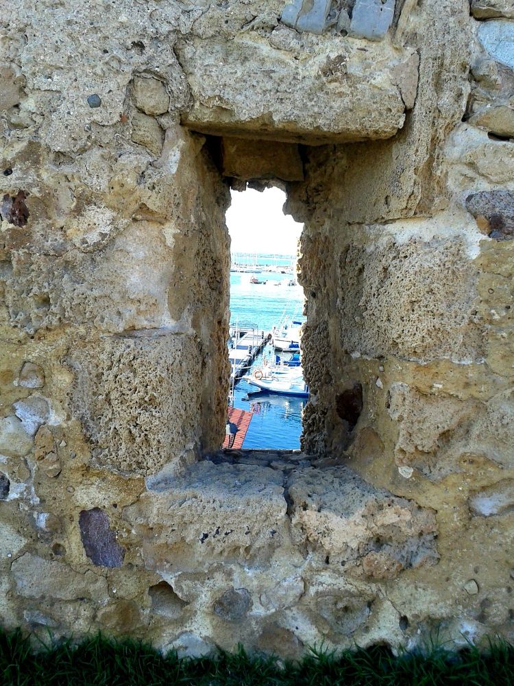 Vertikales Loch in Sandsteinmauer. Blick auf kleinen Hafen mit Segelbooten