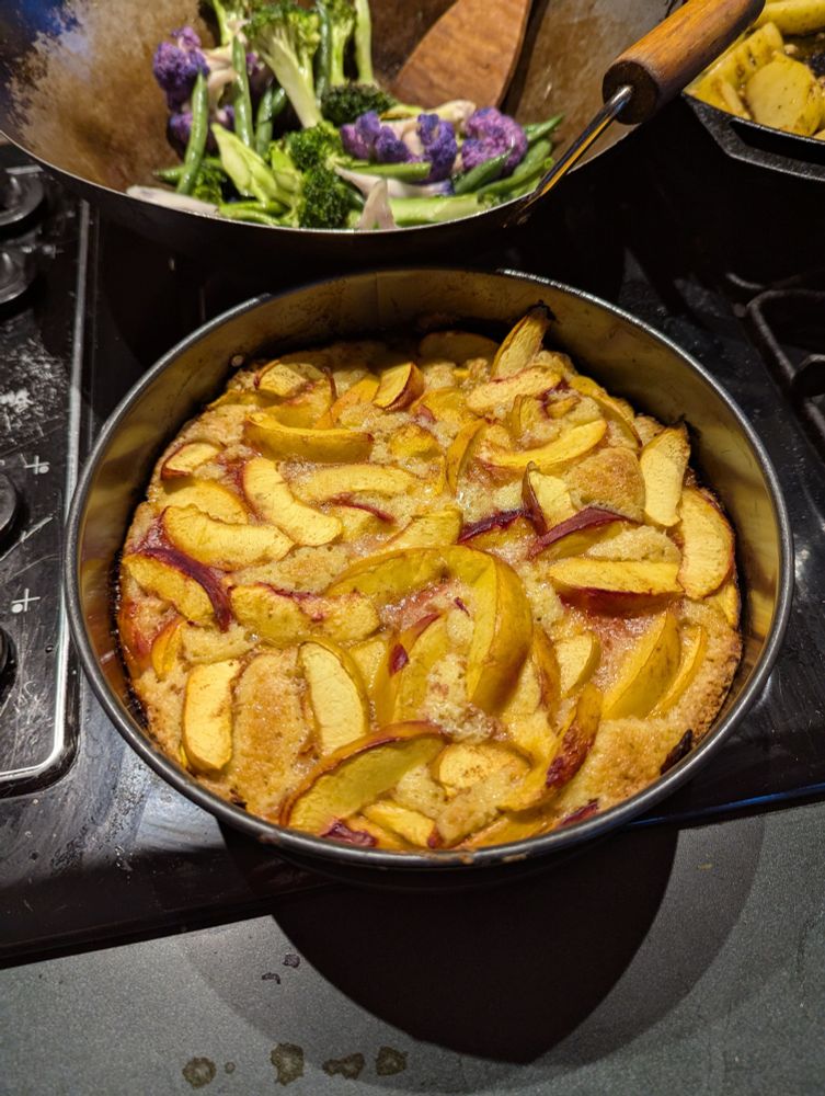 A peach cake in a springform pan on the stovetop. The wok full of the aforementioned veggies is in the background.
