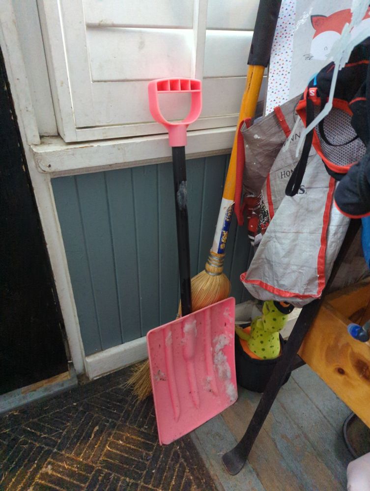 A small pink snow shovel intended for a child's use. In a messy porch.