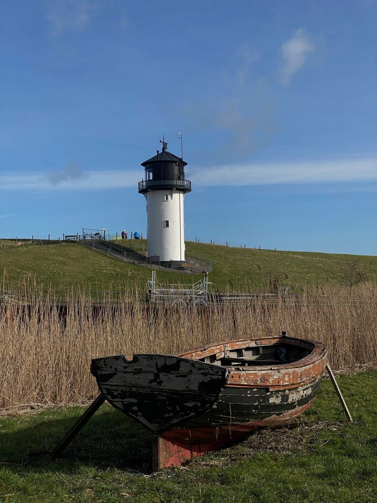 Dicke Berta. Leuchtturm mit altem Holzboot davor. Cuxhaven Altenbruch