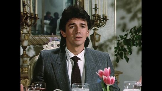 Adrian Zmed with a mullet in a fancy-ass restaurant, looking like a stunned weasel.
