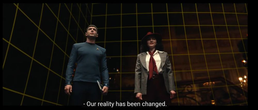 two persons stand in a room with a yellow quadradic grid on black walls