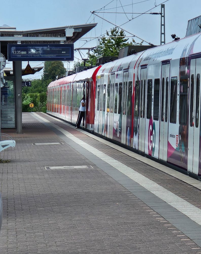 S-Bahn am Bahnsteig.
Alle Türen sind bereits geschlossen, mit Ausnahme einer: Hier stehen zwei Damen in der Tür und blockieren sie.
