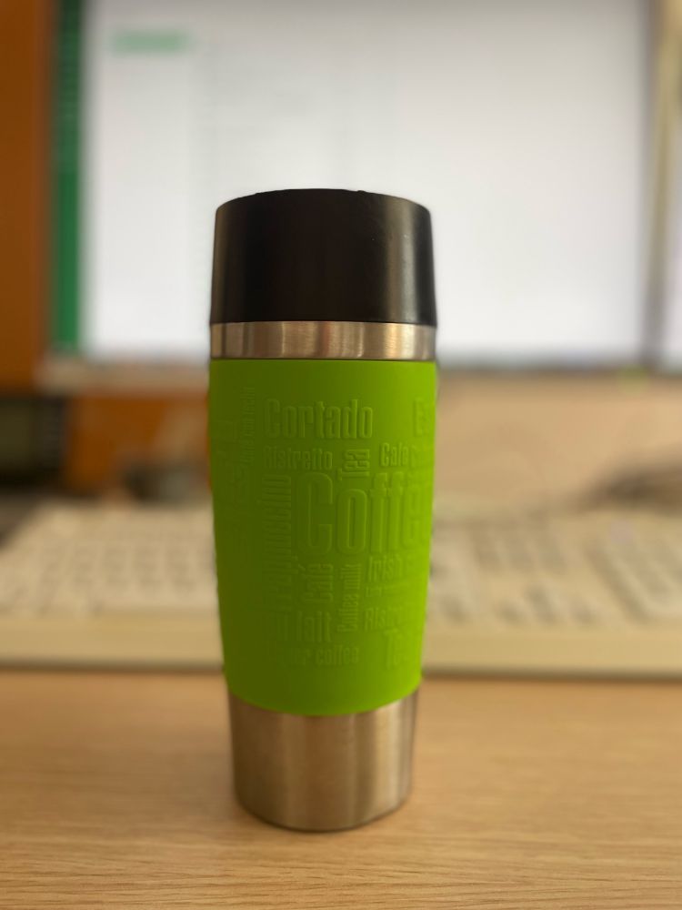 Thermobecher auf Büroschreibtisch gefüllt mit heißem Kaffee.