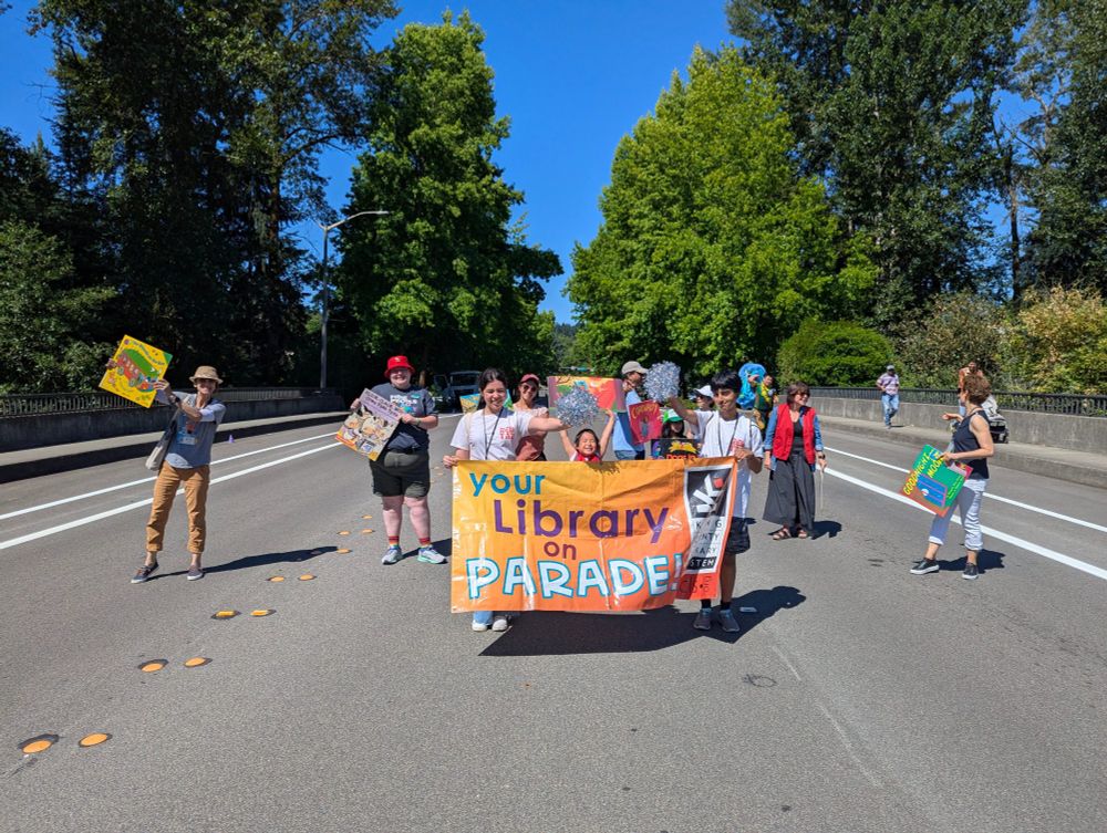 Redmond library staff holding large format books and a banner that reads "Your Library on Parade" at the Redmond Derby Days Parade
