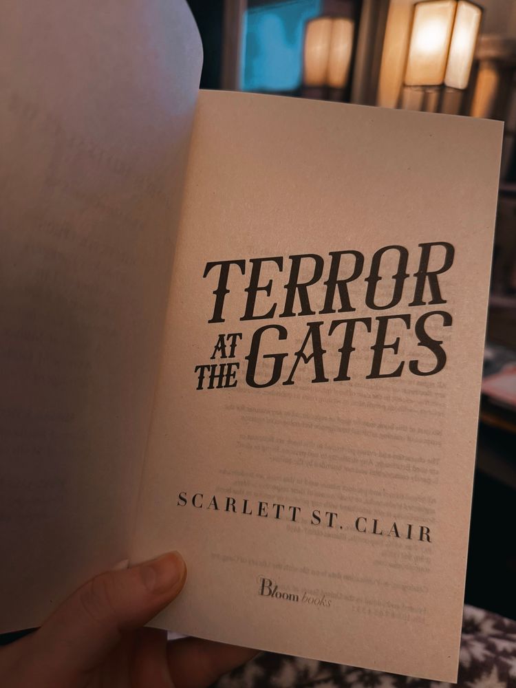 Hand holding book open to title page that reads “terror at the gates by Scarlett st. Clair”

