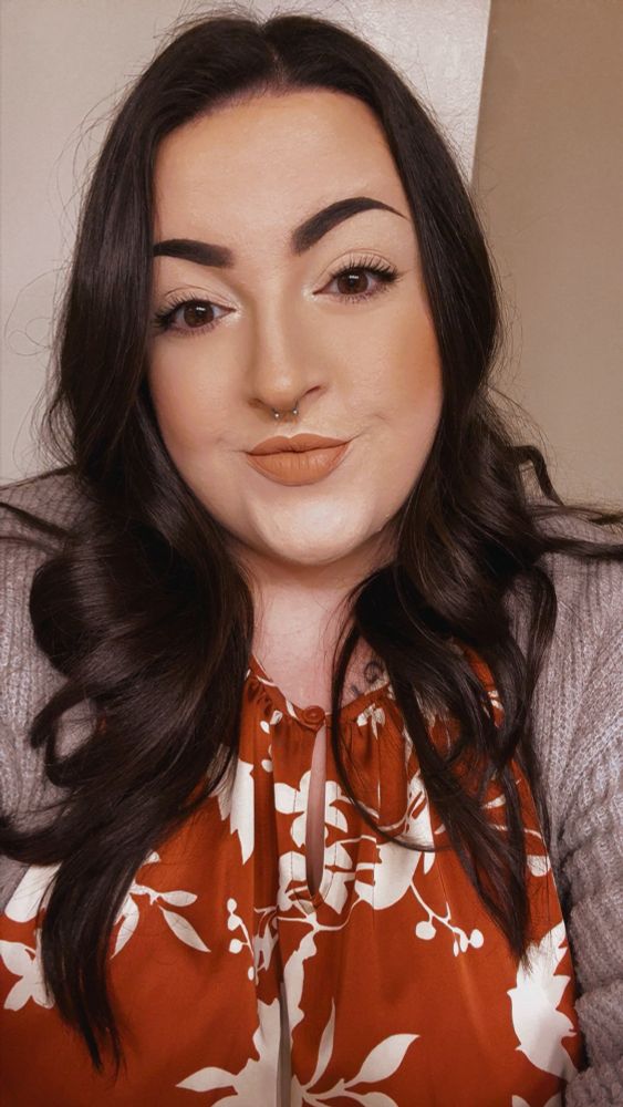 Photo of me with my hair curled smiling at the camera, wearing an orange floral dress and a grey sweater. 