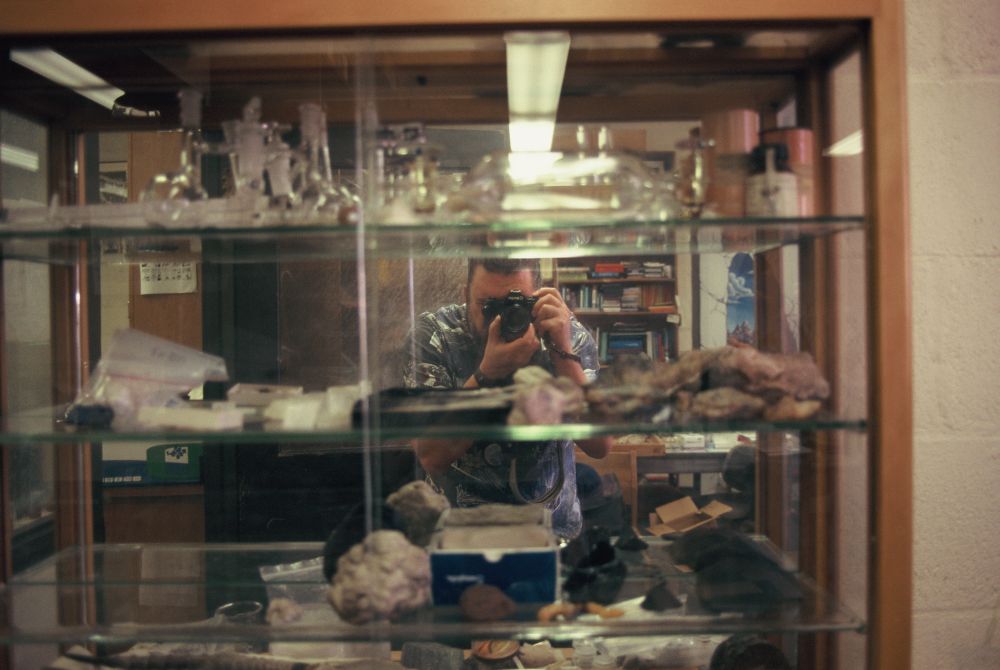 Reflection of the photographer in a mirrored display case containing miscellaneous rocks and geological samples.