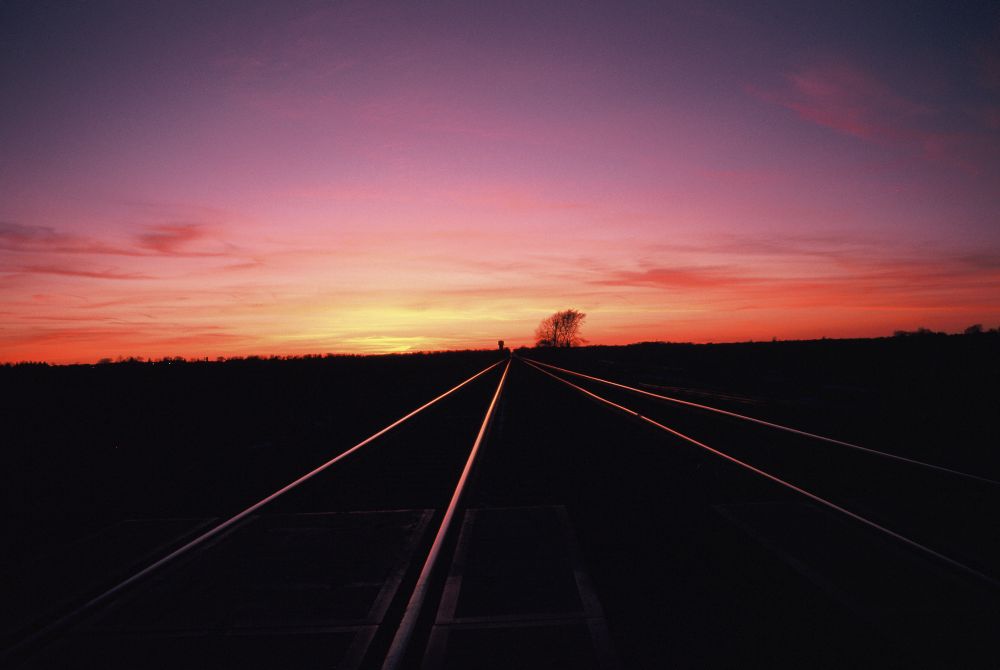 A vibrate sunset with pink and gold hues is reflected on the rails of a railroad in the upper Midwest.