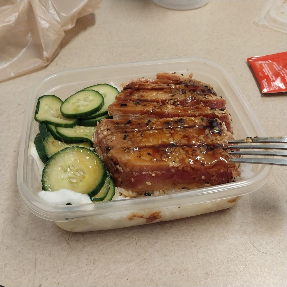 A Tupperware container with sliced tuna steaks, rice and cucumber salad