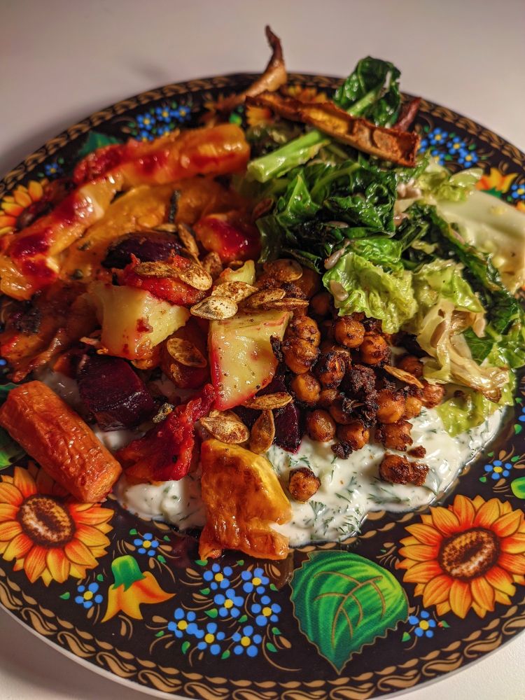 roasted autumn veggies (pumpkin, beet, carrots, sweet & normal potatoes), next to roasted tomato jamaica jerk chickpeas, next to wilted cabbage (some special "curly" type), topped with roasted pumpkin seeds & pumpkin peels, and everything is served on top of vegan tzatziki