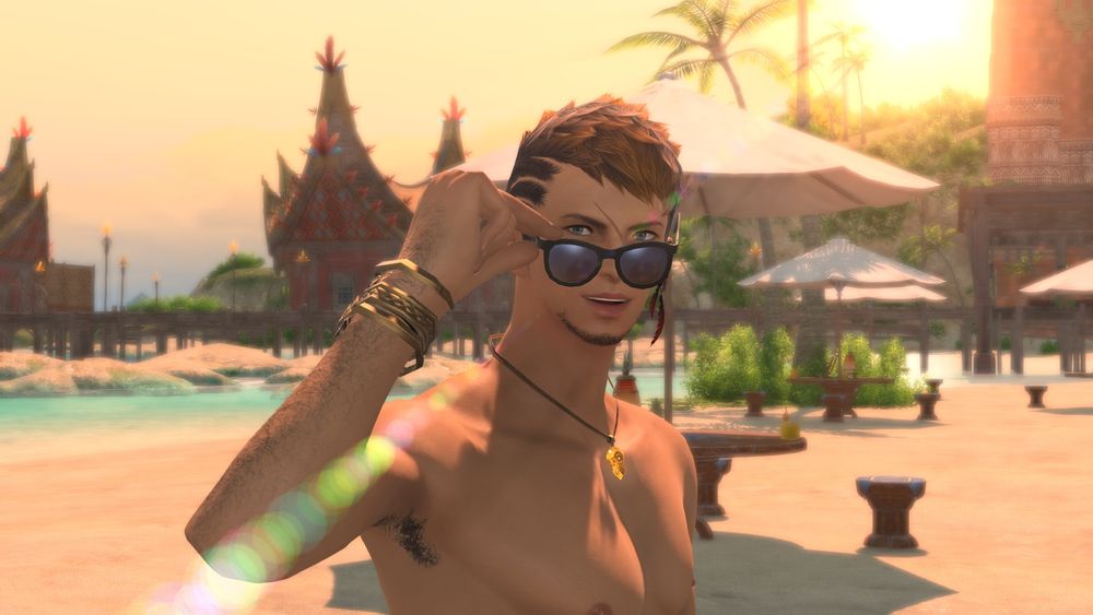 Close-up shot of Fin on a beach in Tuliyollal, looking at the viewer, his sunglasses held a bit away from his face. The sun is setting in the background. There's a lens flare which makes it 10x cooler.