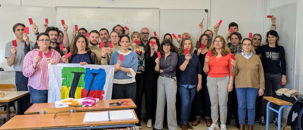 Photo d'un rassemblement des personnels du lycée français de Barcelone, brandissant des cartons rouge. Il y a un drapeau FSU et noté "attention dialogue social"