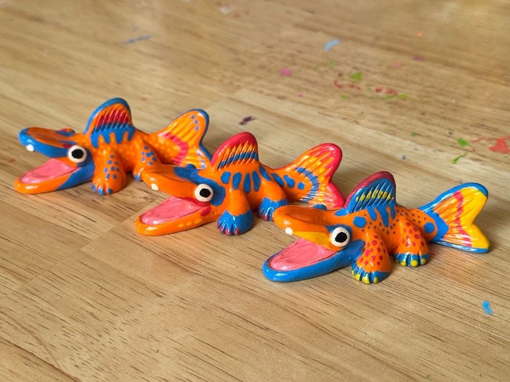 Photo of three fish creature figurines on a table. Their bodies are painted with various patterns using orange, blue, red, and yellow