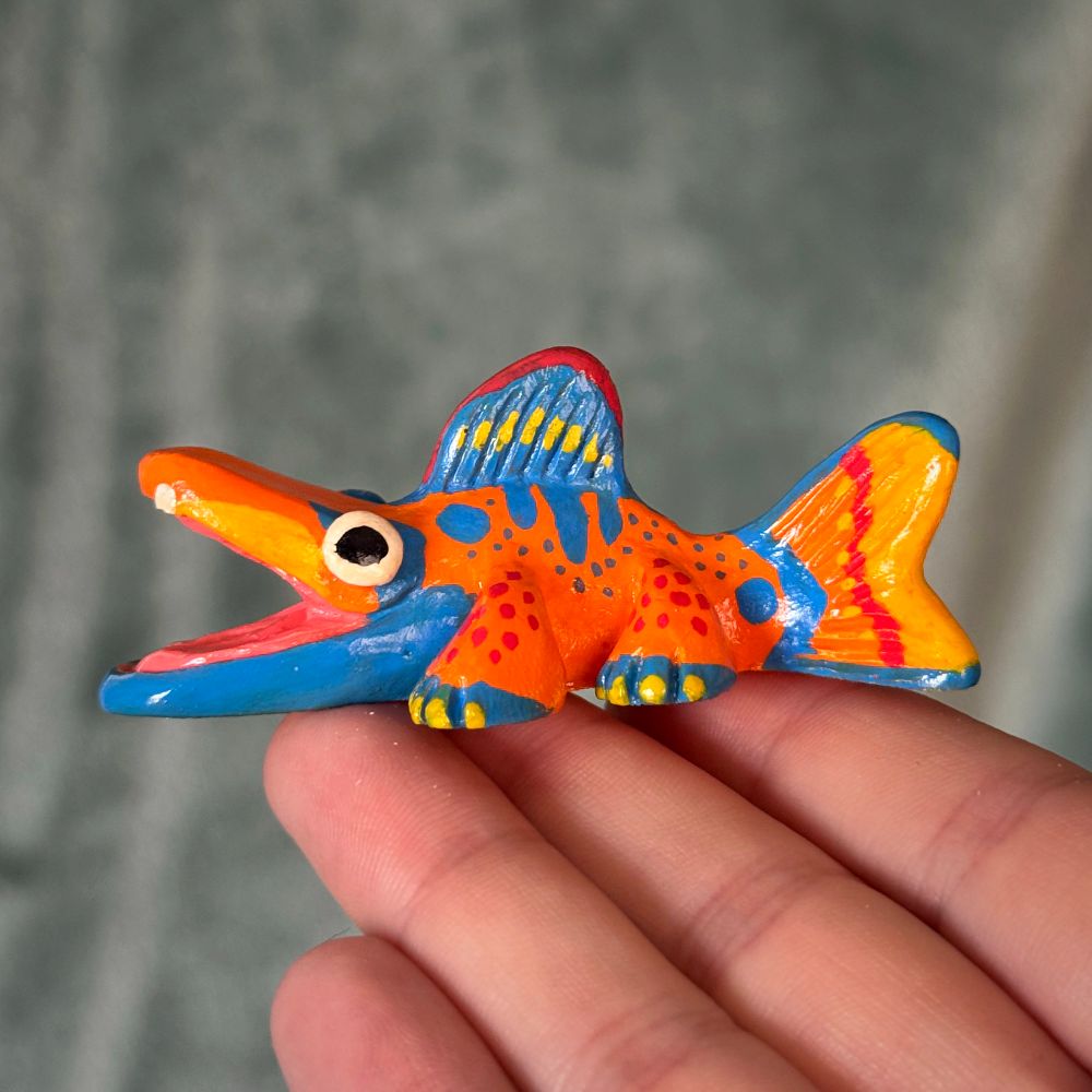 Photo of a creature figurine. The creature is fish-like with legs. It is painted with orange, blue, red, and yellow patterns