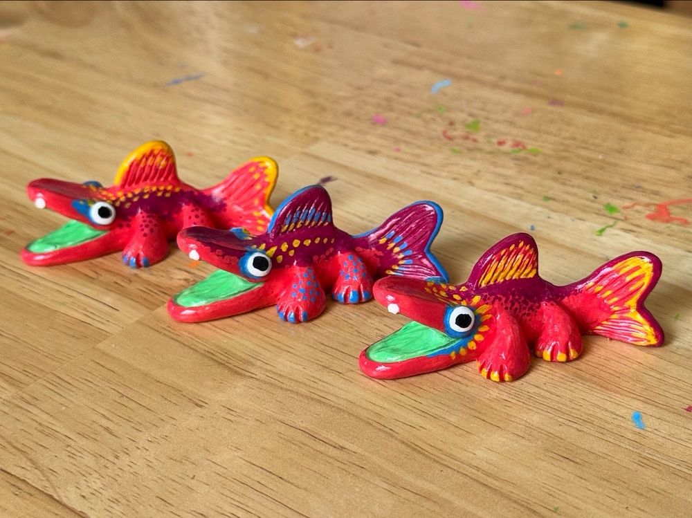 Photo of three fish creature figurines on a table. Their bodies are painted with various patterns using red, blue, and yellow