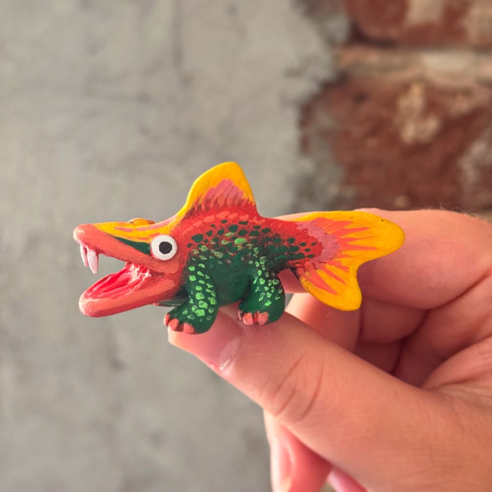 Photo of a creature sculpture being held. The sculpture is a painted clay model of a fish-like creature with legs