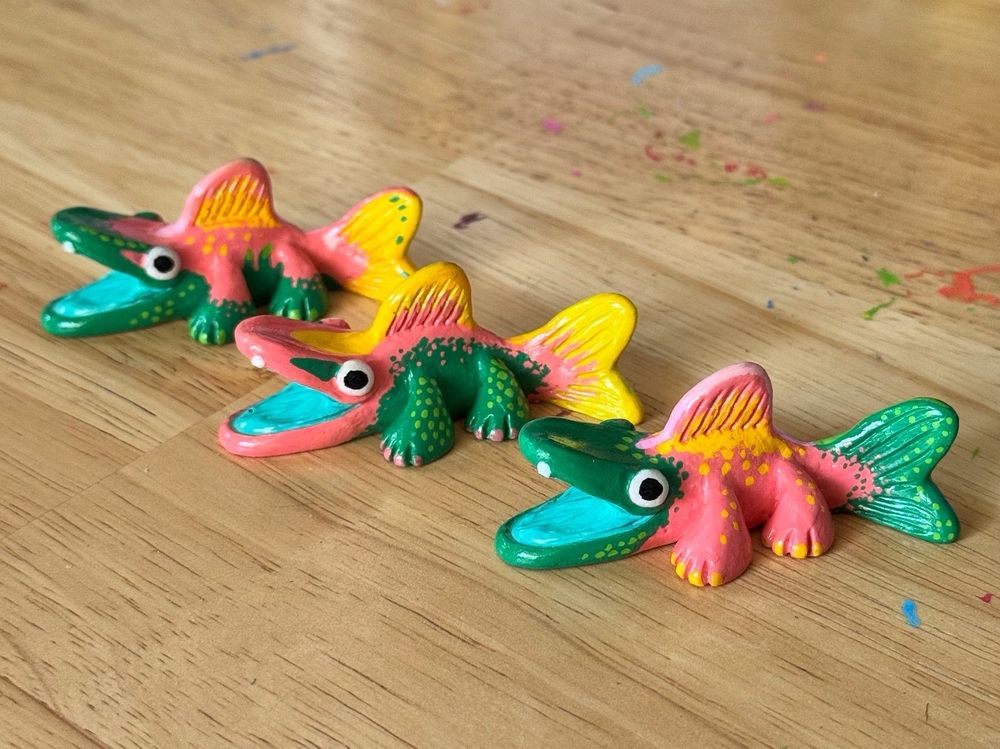 Photo of three fish creature figurines on a table. Their bodies are painted with various patterns using pink, green, and yellow