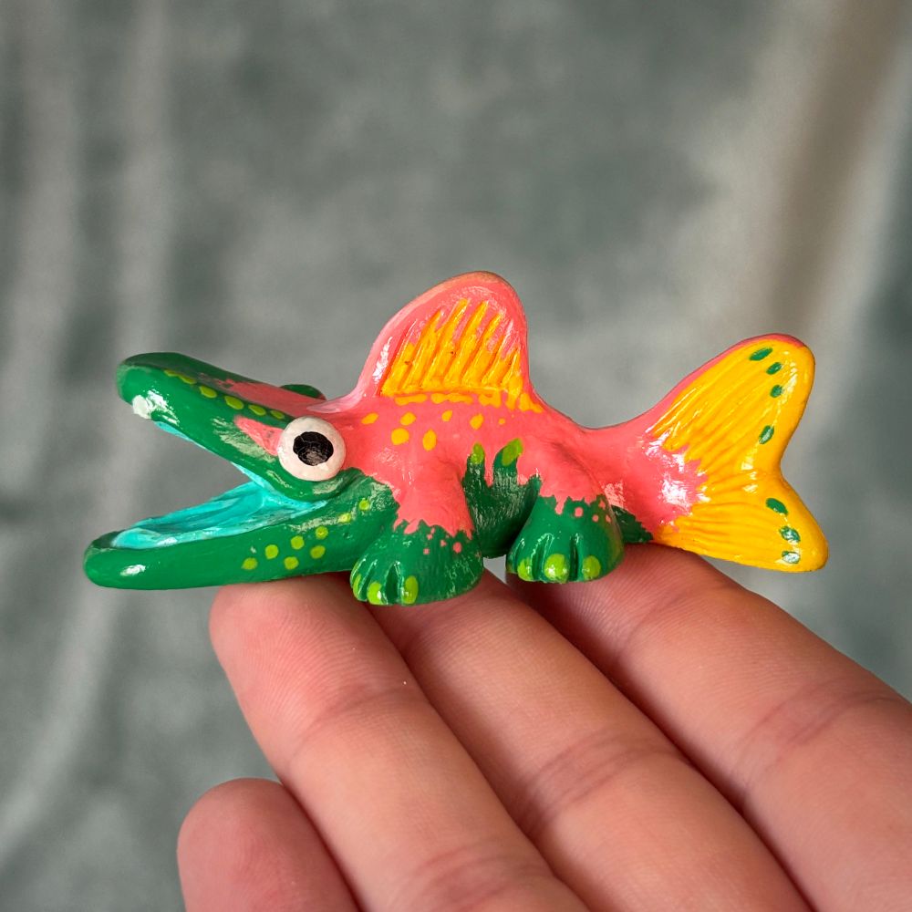 Photo of a creature figurine. The creature is fish-like with legs. It is painted with green, pink, and yellow patterns