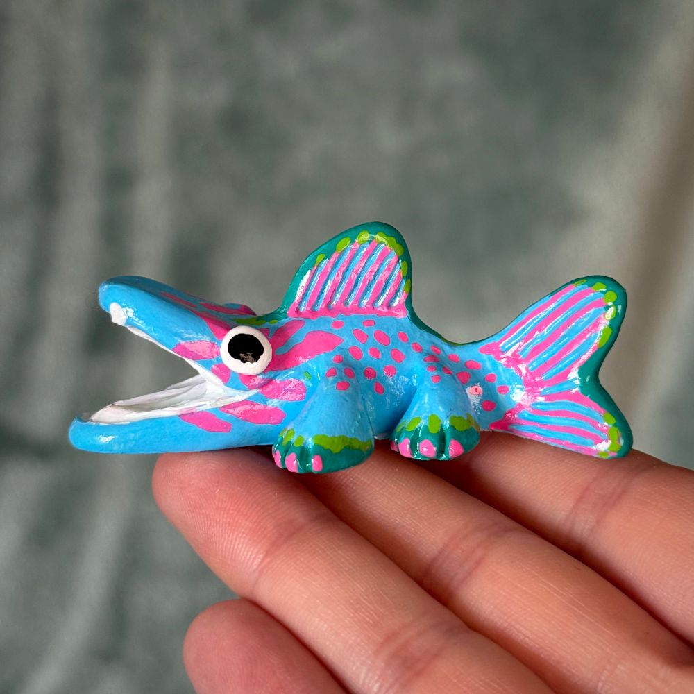 Photo of a creature figurine. The creature is fish-like with legs. It is painted with blue, green, and pink patterns
