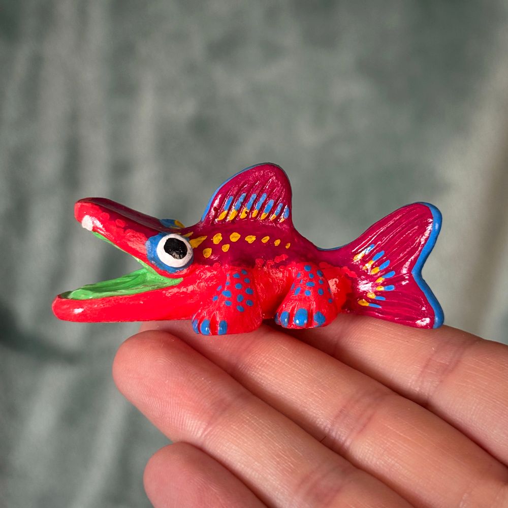 Photo of a creature figurine. The creature is fish-like with legs. It is painted with red, yellow, and blue patterns