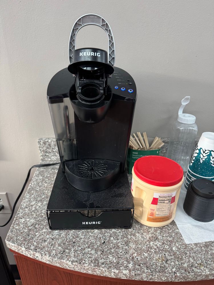 A keurig coffeemaker and a giant Costco container of coffee mate on a faux-granite counter, an abomination in the sight of God 