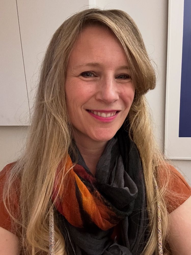 Me wearing an orange jumpsuit and grey and orange scarf. I’m smiling. It’s a selfie.