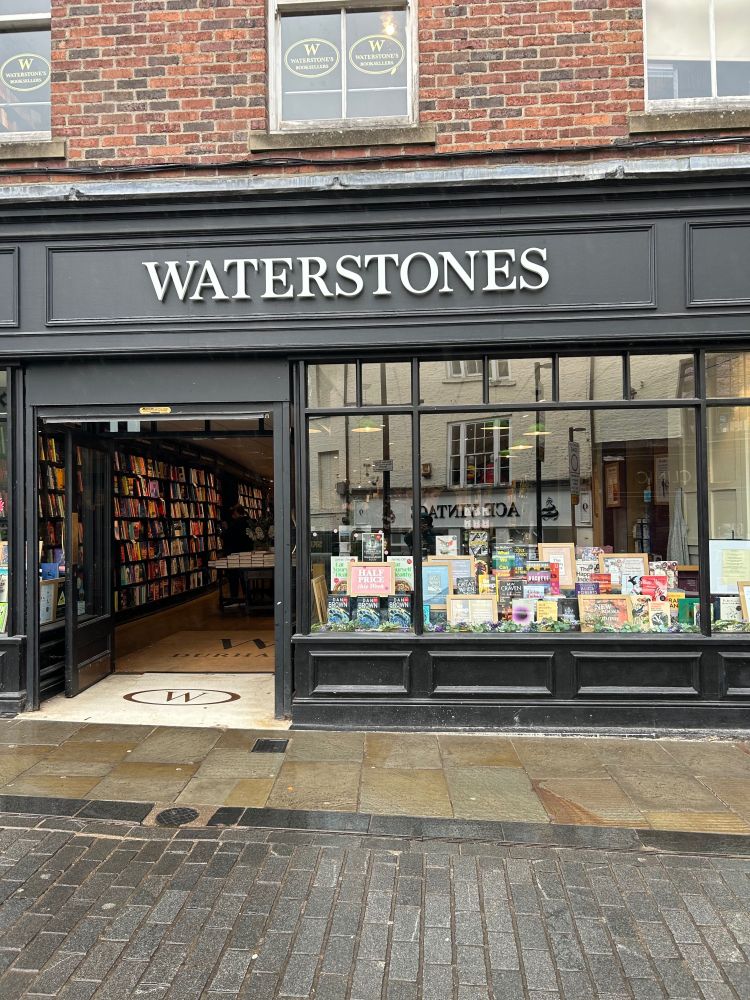 A photo I took of the outside of the Waterstones in Durham. The building is painted black and the lettering is in white. There are large windows with books displayed in them.